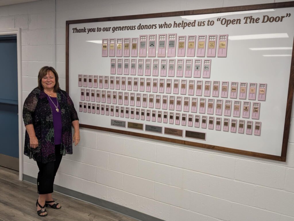 A woman standing beside a donor recognition wall.
