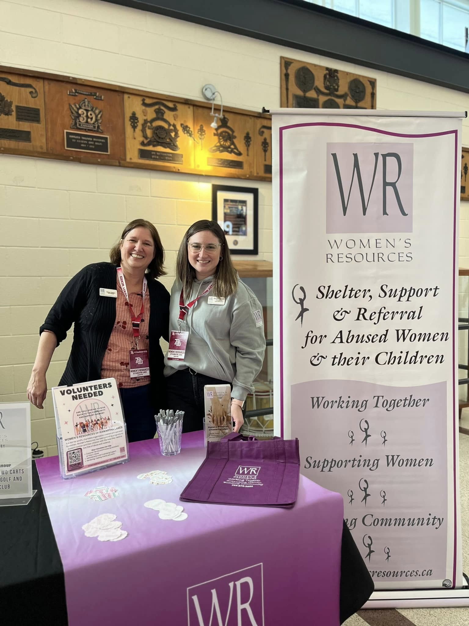 Two Women's Resources employees posing for a photo in front of Women's Resources signage and banners.